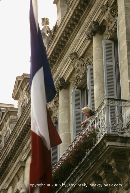 woman watches parade from her balcony over Place Verdun