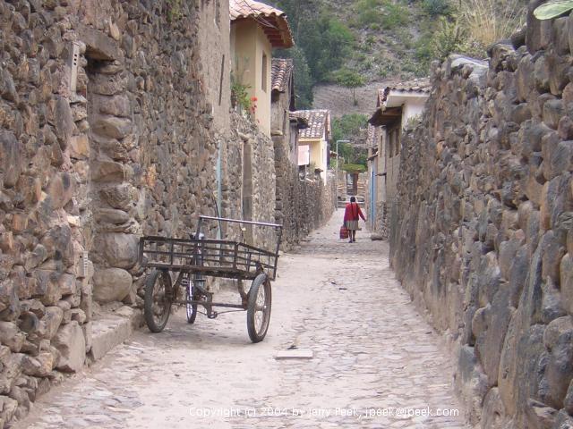 Bicycle-drawn cart and woman walking along stone-walled street, Ollantaytambo, Peru