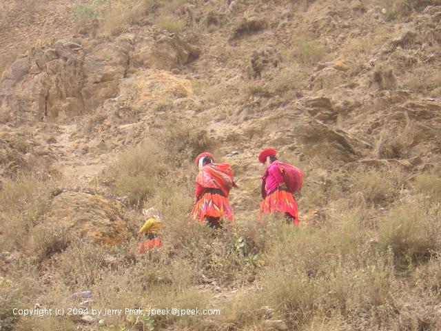 Three people in bright-colored clothes walking up a path, Ollantaytambo, Peru