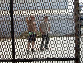 Two men looking at border fence from Mexican side