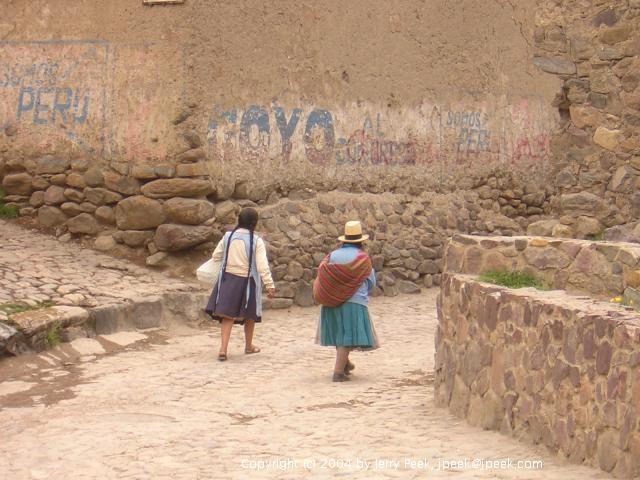 Women walking under a wall with advertising (and graffiti?), Ollantaytambo, Peru